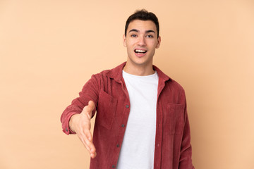 Young caucasian handsome man isolated on beige background shaking hands for closing a good deal