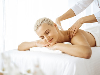 Beautiful blonde woman enjoying back massage with closed eyes. Spa salon concept