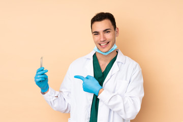 Young dentist man holding tools isolated on beige background holding copyspace imaginary on the...
