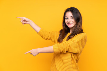 Young caucasian woman isolated on yellow background pointing finger to the side and presenting a product