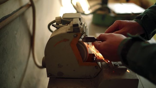Worker sharpening a chisel on a sharpening machine. Woodworker sharpening chisel with grindstone abrasive disc cutter machine