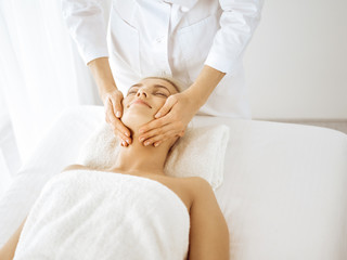 Fototapeta na wymiar Beautiful blonde woman enjoying facial massage with closed eyes. Relaxing treatment in medicine and spa center concepts