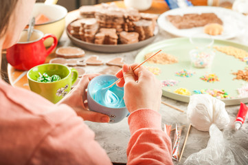 The process of coloring ginger Easter gingerbread cookies close-up. Mixing aisings for gingerbread cookies in the form of bunnies and eggs. Hands mix cream and copy space.