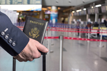 Man (businessman)  in a blue suit with suitcase holding american passport in the airport opposite check-in area. concept. America. USA