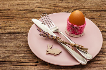 Easter table setting on vintage wooden boards background. Spring holiday card template. Cutlery, egg, lavender, bunny, knitted stand