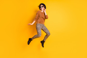 Fototapeta na wymiar Full body photo of crazy excited lady jump high up rejoicing vacation weekend abroad wear soft sweater leopard pants specs retro cap footwear isolated yellow color background