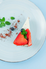 A beautiful piece of cake with berries with butter cream on a blue background. Cake with red cakes.