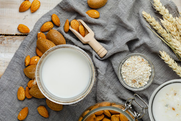 Fresh vegan alternative milk in big glass. Closeup, wooden background. Healthy vegetarian food concept, delicious low calorie drink. Almond, hazelnut, oatmeal, rice as ingredients. Flat lay, top view