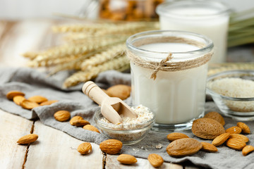 Fresh vegan alternative milk in big glass. Closeup, wooden background. Healthy vegetarian food concept, delicious low calorie drink. Almond, hazelnut, oatmeal, rice to illustrate raw ingredients. 
