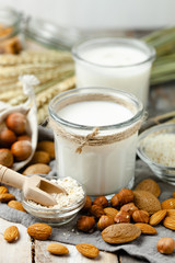 Fresh vegan alternative milk in big glass. Closeup, wooden background. Healthy vegetarian food concept, delicious low calorie drink. Almond, hazelnut, oatmeal, rice to illustrate raw ingredients. 