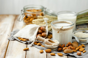 Fresh vegan alternative milk in big glass. Closeup, wooden background. Healthy vegetarian food concept, delicious low calorie drink. Almond, hazelnut, oatmeal, rice to illustrate raw ingredients. 