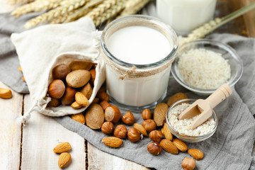 Fresh vegan alternative milk in big glass. Closeup, wooden background. Healthy vegetarian food concept, delicious low calorie drink. Almond, hazelnut, oatmeal, rice to illustrate raw ingredients. 