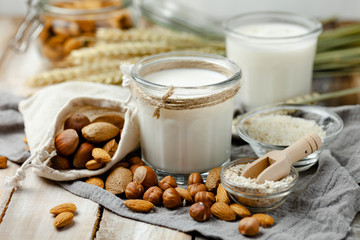 Fresh vegan alternative milk in big glass. Closeup, wooden background. Healthy vegetarian food concept, delicious low calorie drink. Almond, hazelnut, oatmeal, rice to illustrate raw ingredients. 