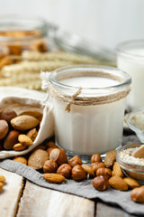 Fresh vegan alternative milk in big glass. Closeup, wooden background. Healthy vegetarian food concept, delicious low calorie drink. Almond, hazelnut, oatmeal, rice to illustrate raw ingredients. 