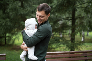 portrait of smiling brunette dad in green jacket with baby in his arms in Park