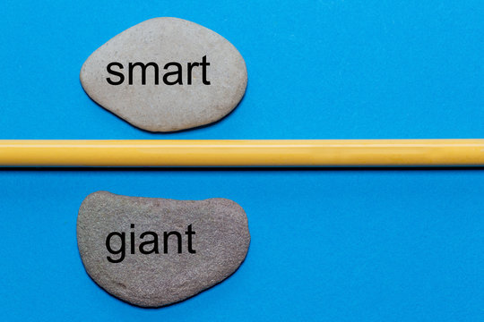 The words smart and giant are written on natural smooth stones separated by a yellow pencil. The background is isolated in blue and has a lot of space