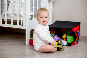 baby in white clothes is sitting on the floor in the children's room and playing with toys