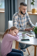 Sad daughter resting her head in her arms, on the table.