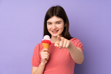 Young Ukrainian teenager girl holding a cornet ice cream over isolated purple background points finger at you with a confident expression