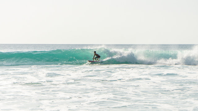 View of a silhouette of a boy surfin' the waves at sunset in Bali, Indonesie