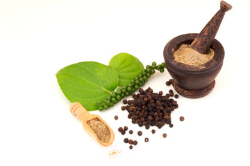 Black peppercorns scattered and herbs in mortar