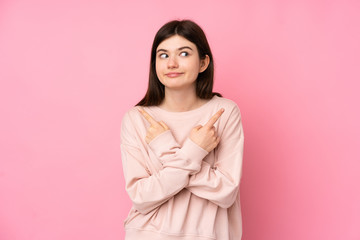Fototapeta premium Young Ukrainian teenager girl over isolated pink background pointing to the laterals having doubts