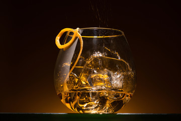 transparent glass with citrus peel, ice cubes and vodka in dark with warm back light