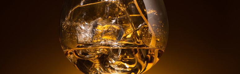 transparent glass with ice cubes and vodka in dark with warm back light, panoramic shot