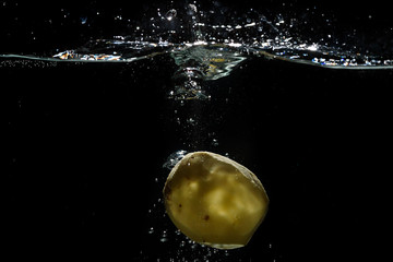 Potato thrown into the water for cooking with splashes of water on a black background