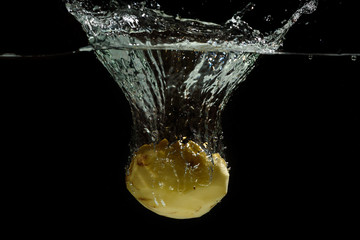 Potato thrown into the water for cooking with splashes of water on a black background - Powered by Adobe
