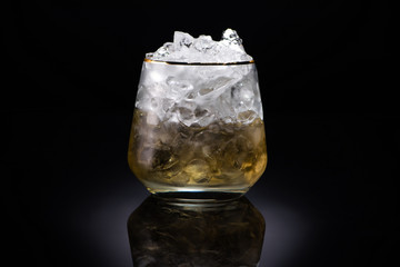 transparent glass with ice and golden liquid on black background