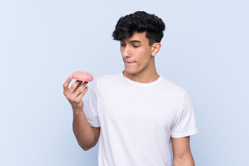 Young Argentinian man over isolated blue background holding a donut