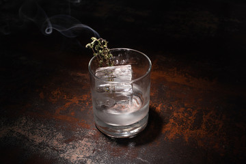 transparent glass with burning herb, ice cube and vodka on weathered surface