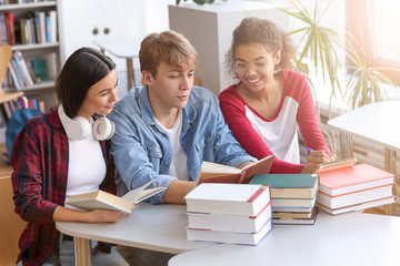 Young students reading books while preparing for exam in library