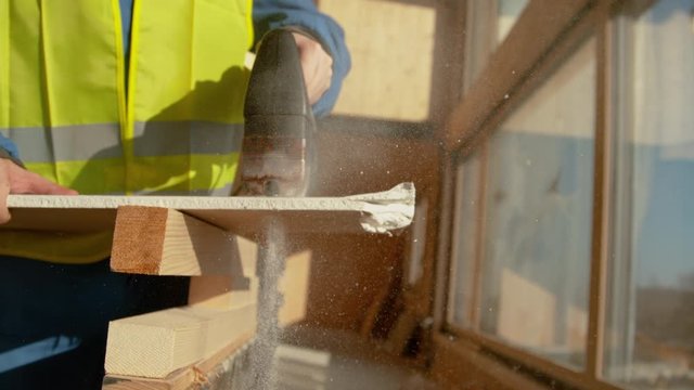 SUPER SLOW MOTION, CLOSE UP, DOF: Unrecognizable builder in a bright yellow safety vest cuts a plasterboard with a rusty jigsaw. Experienced contractor at a construction site cutting sheets of plaster