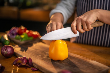 Female chef is about to start slicing a fresh yellow pepper on a wooden cutting board in a kitchen or restaurant.