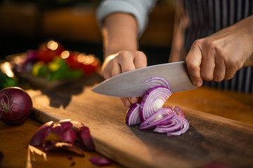 Female chef is precisely slicing red onions on a wooden cutting board in a restaurant. 