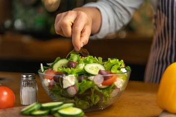 Woman chef is putting final decorations on a bowl of freshly made, organic, tasty salad.