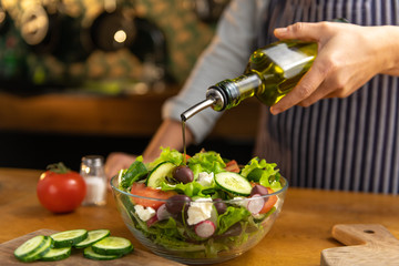 Woman chef is pouring olive oil on a glass bowl of freshly made tasty, organic diet salad.