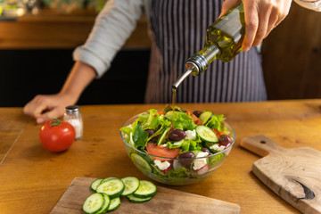 Woman chef is pouring olive oil on a glass bowl of freshly made tasty, organic diet salad.