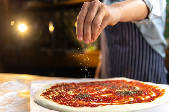 Female chef is sprinkling fresh oregano over a traditionally made home pizza. 
