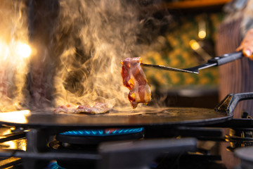 Close up of a female chef flipping a sizzling, hot pieces of bacon on a kitchen stove. 