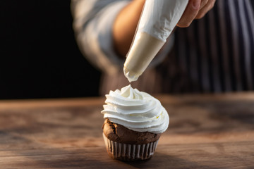 Extreme close up of a chef pouring whipped cream over a freshly baked cupcake
