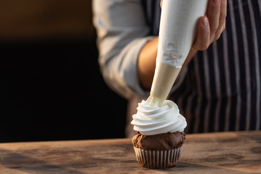 Close up of a chef pouring whipped cream over a freshly baked cupcake