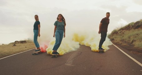 Three stylish carefree friends skateboarding at sunset with colorful smoke trails, fun skateboarding with smoke grenades