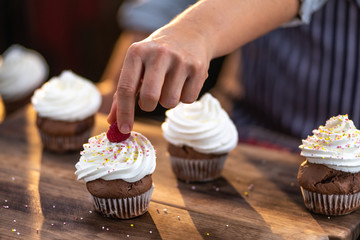 Female hand putting a raspberry on a freshly baked, tasty, delicious cupcake.