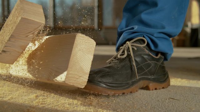 SLOW MOTION, CLOSE UP, DOF: Detailed shot of a painful work accident as a heavy plank falls on an unrecognizable worker's foot. Worker sawing wood drops a beam on his foot. Construction site accident