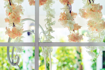 Beautiful artificial flowers hung on glass windows to decorate for a garden party. View from the window on the glass.