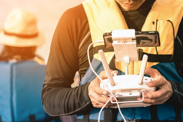 Young man in blue and yellow life vest controlling a drone to take pictures of ocean coast with tourists while traveling on a raft in the sea. Hands holding drone remote controller.