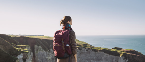 Young tourist woman with backpack looking at sea in Normandy, France over beautiful cliffs background. Travel, active lifestyle and winter holiday concept
